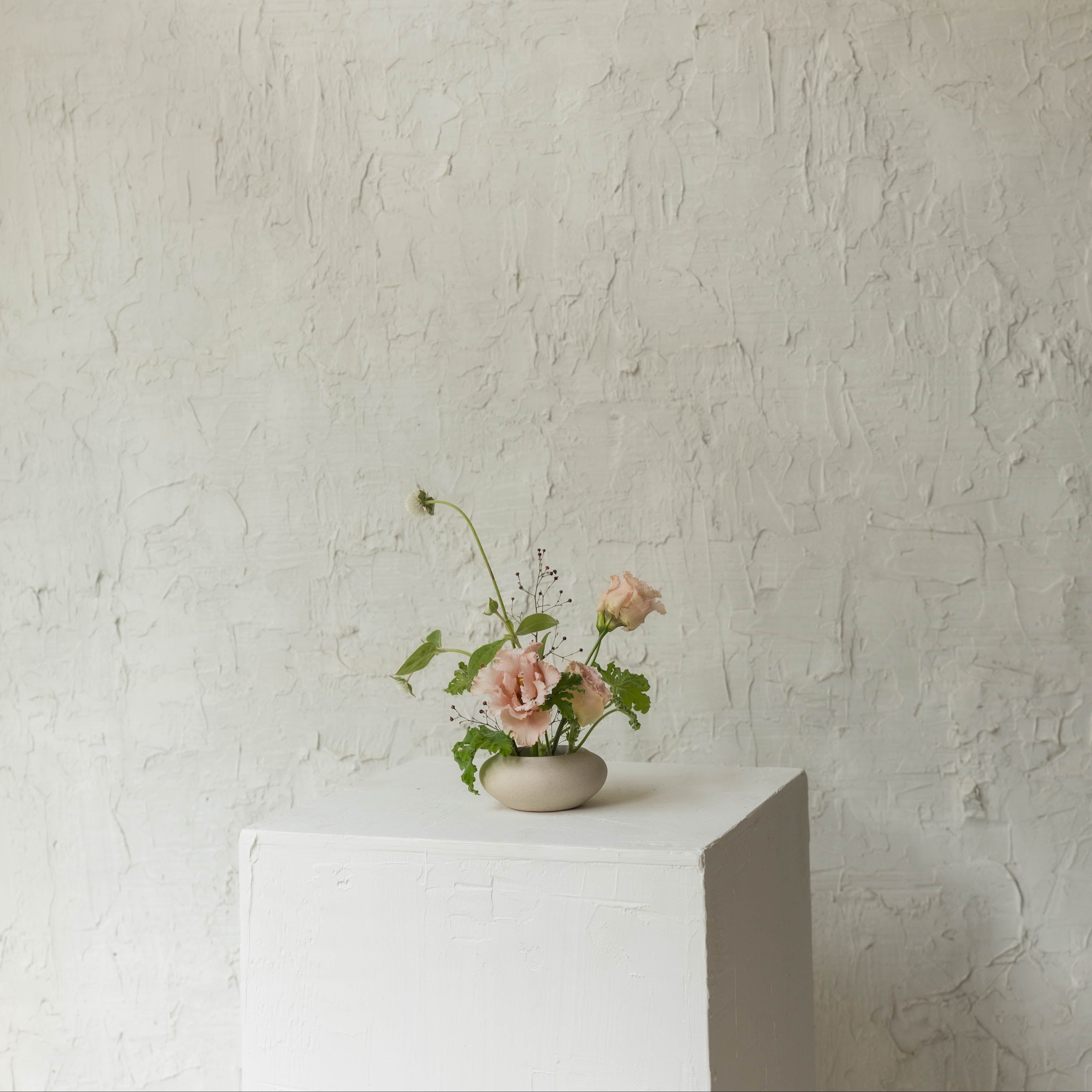 Small vase with flowers on a white pedestal against a textured beige wall