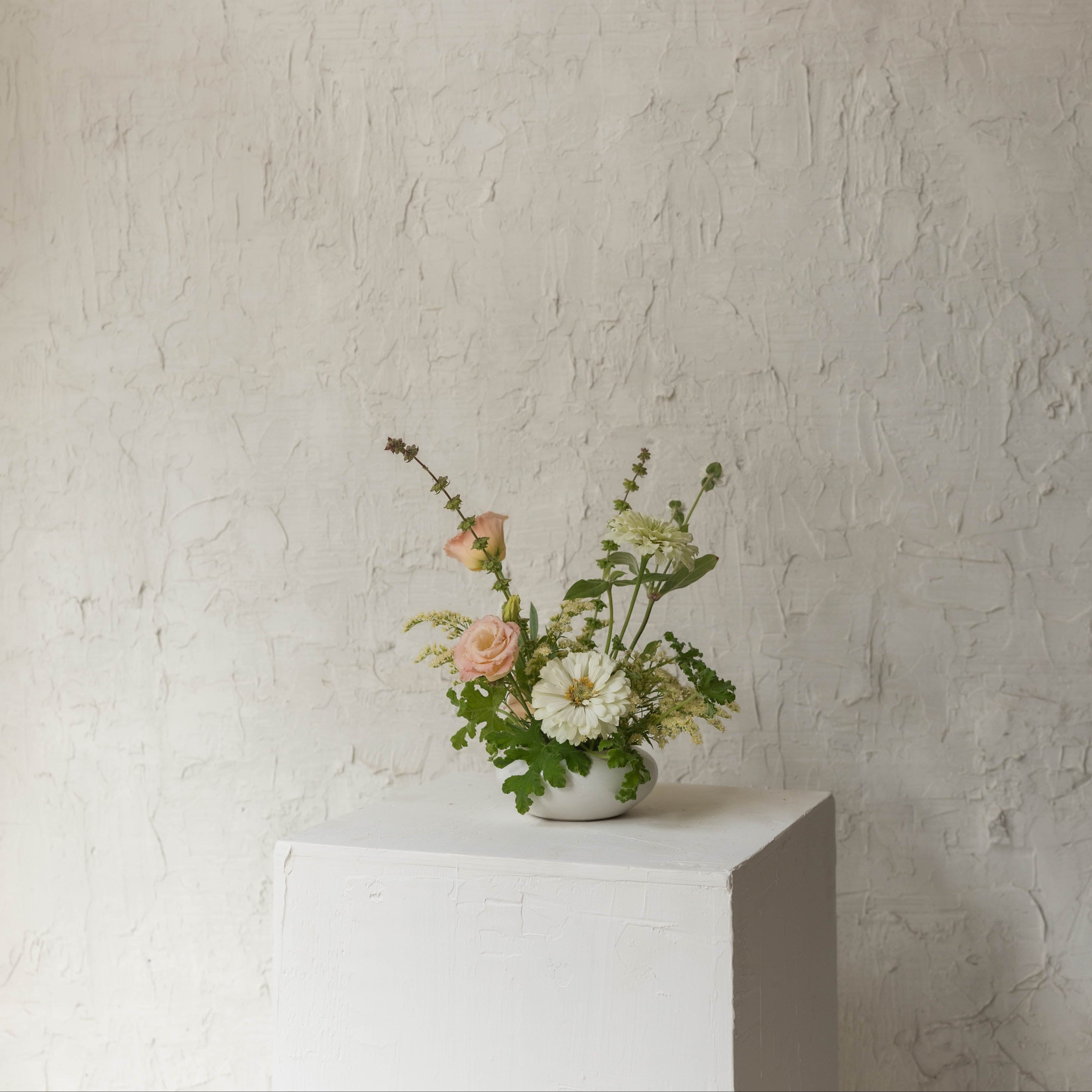 Small floral arrangement on a white pedestal against a textured beige wall