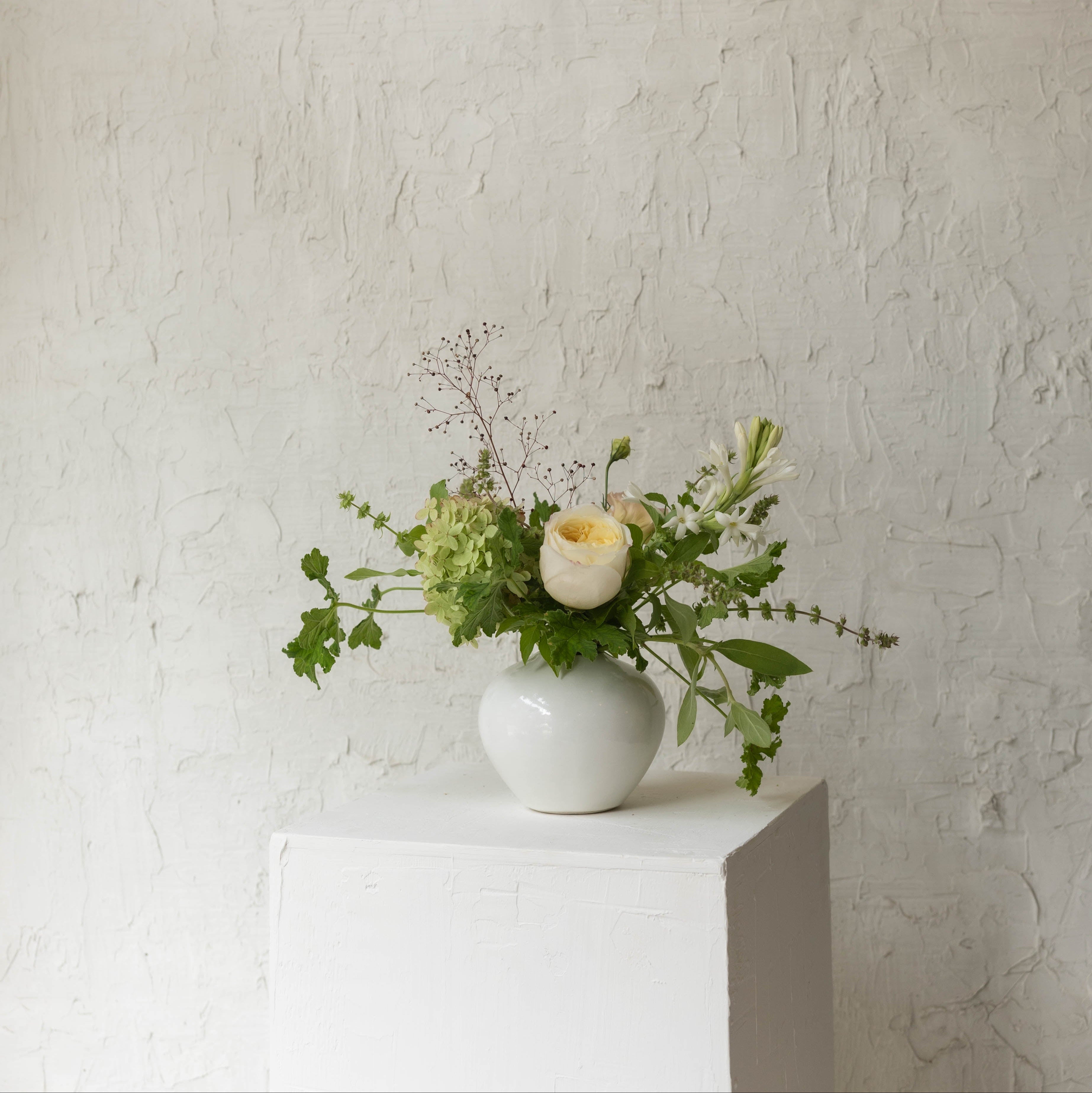Vase with flowers on a white pedestal against a textured white wall