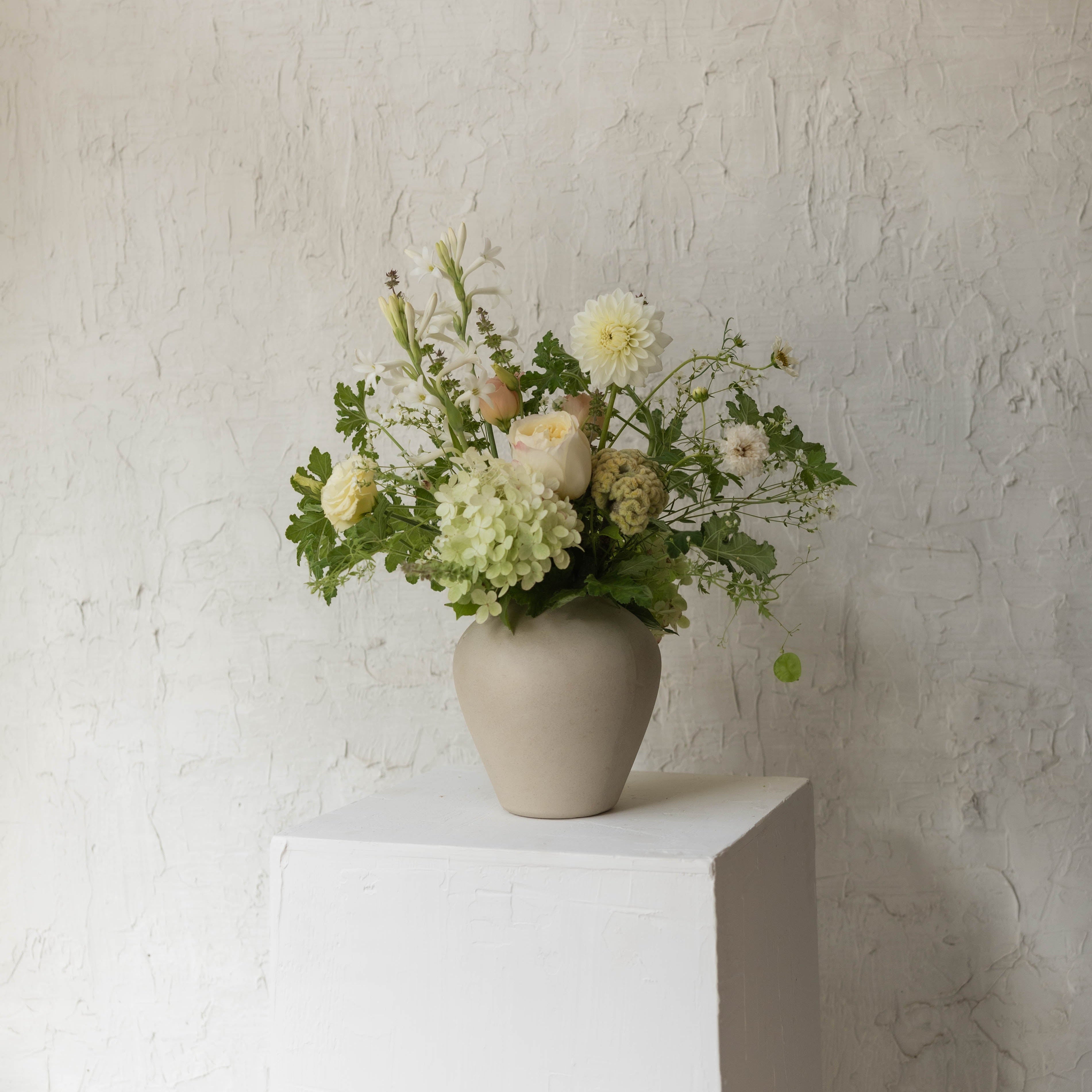 Floral arrangement in a vase on a white pedestal against a textured wall.