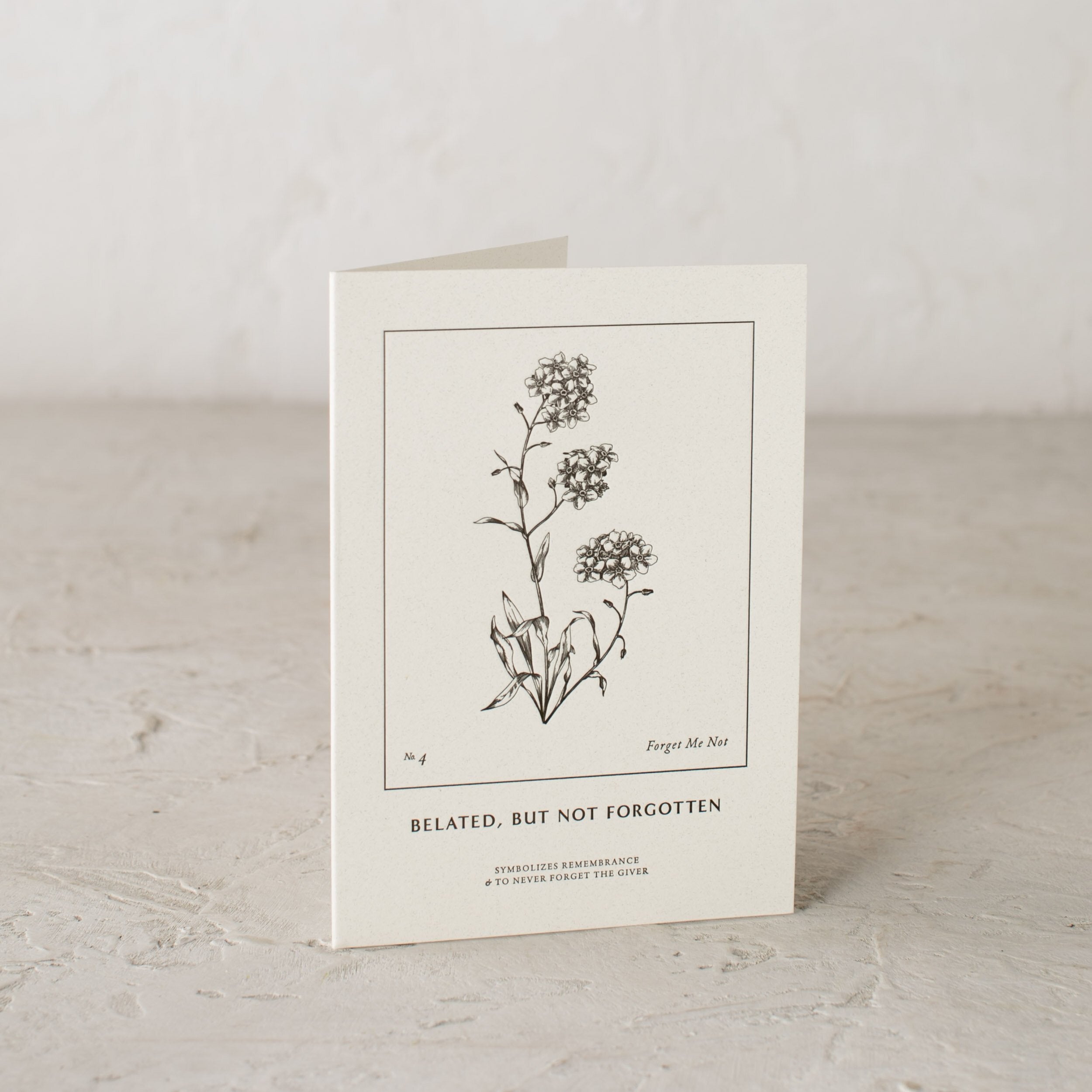 Illustrated botanical embossed card, forget me not. "Belated, but not forgotten " symbolizes remembrance and to never forget the giver. Designed and sold by Shop Verdant, Kansas City gift store.
