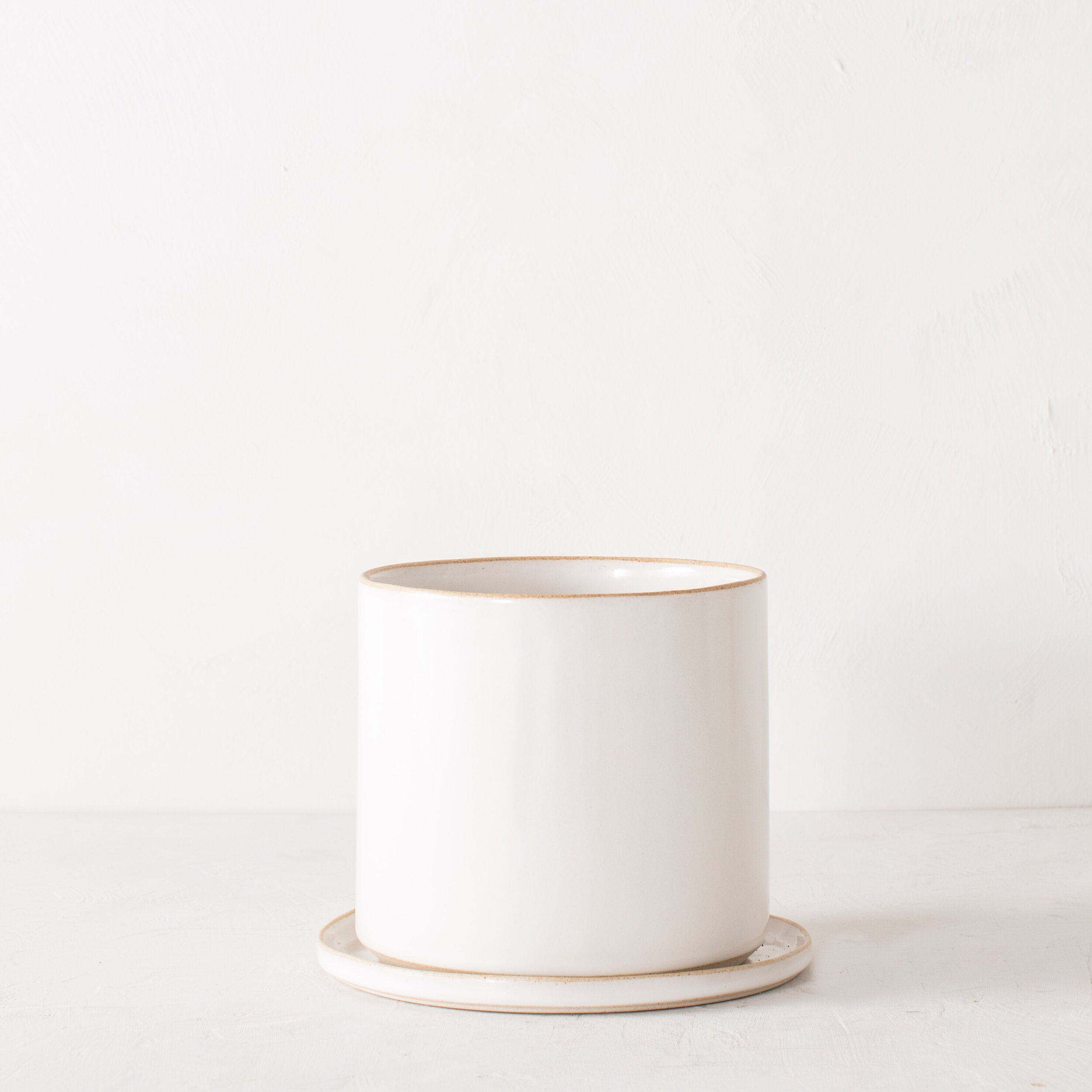 8 inch white ceramic planter with a bottom drainage dish. Staged on a white plaster textured tabletop against a plaster textured white wall. Designed by Convivial Production, sold by Shop Verdant, Kansas City, Mo plant store.