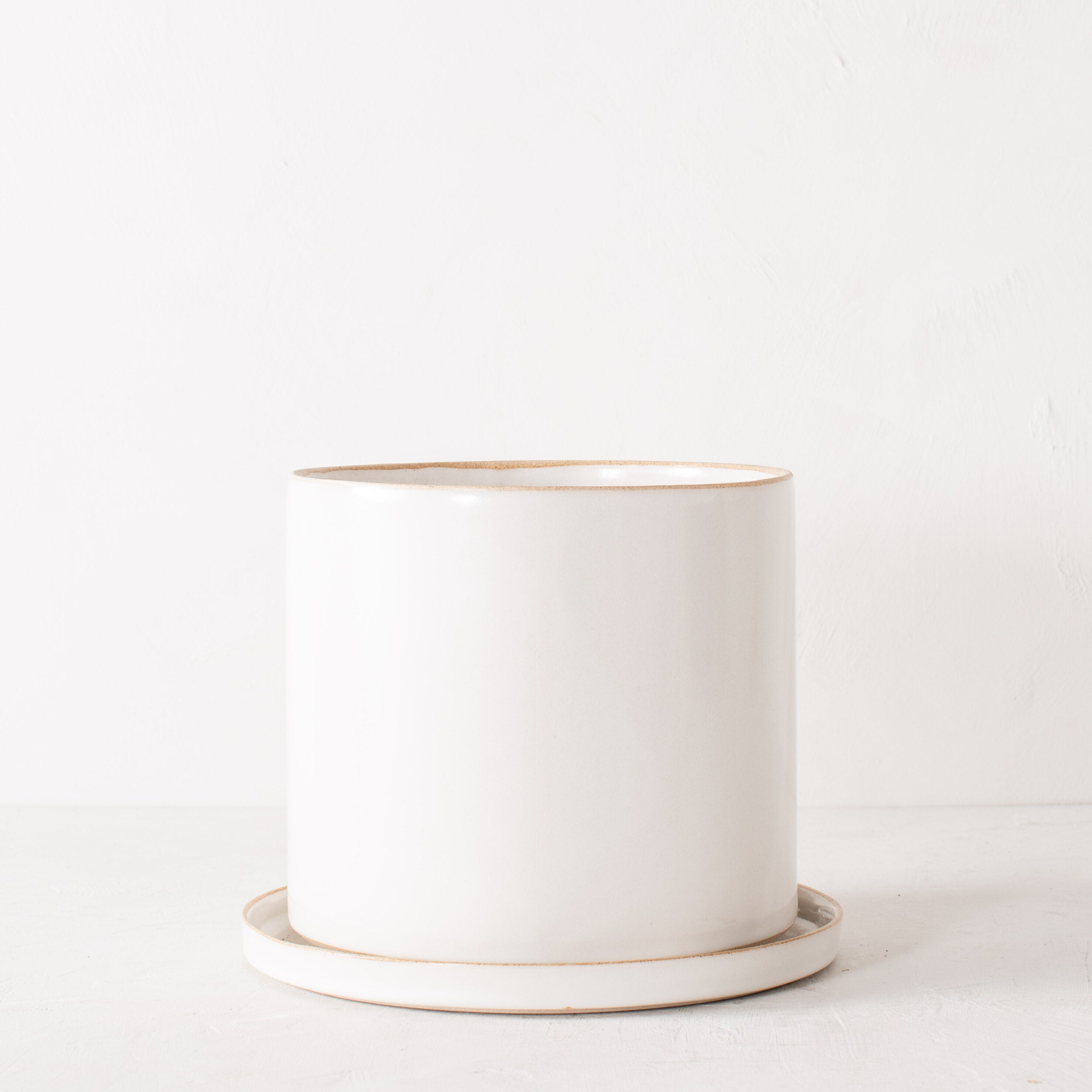 10 inch white ceramic planter with a bottom drainage dish. Staged on a white plaster textured tabletop against a plaster textured white wall. Designed and sold by Convivial Production, Kansas City Ceramics.  Edit alt text