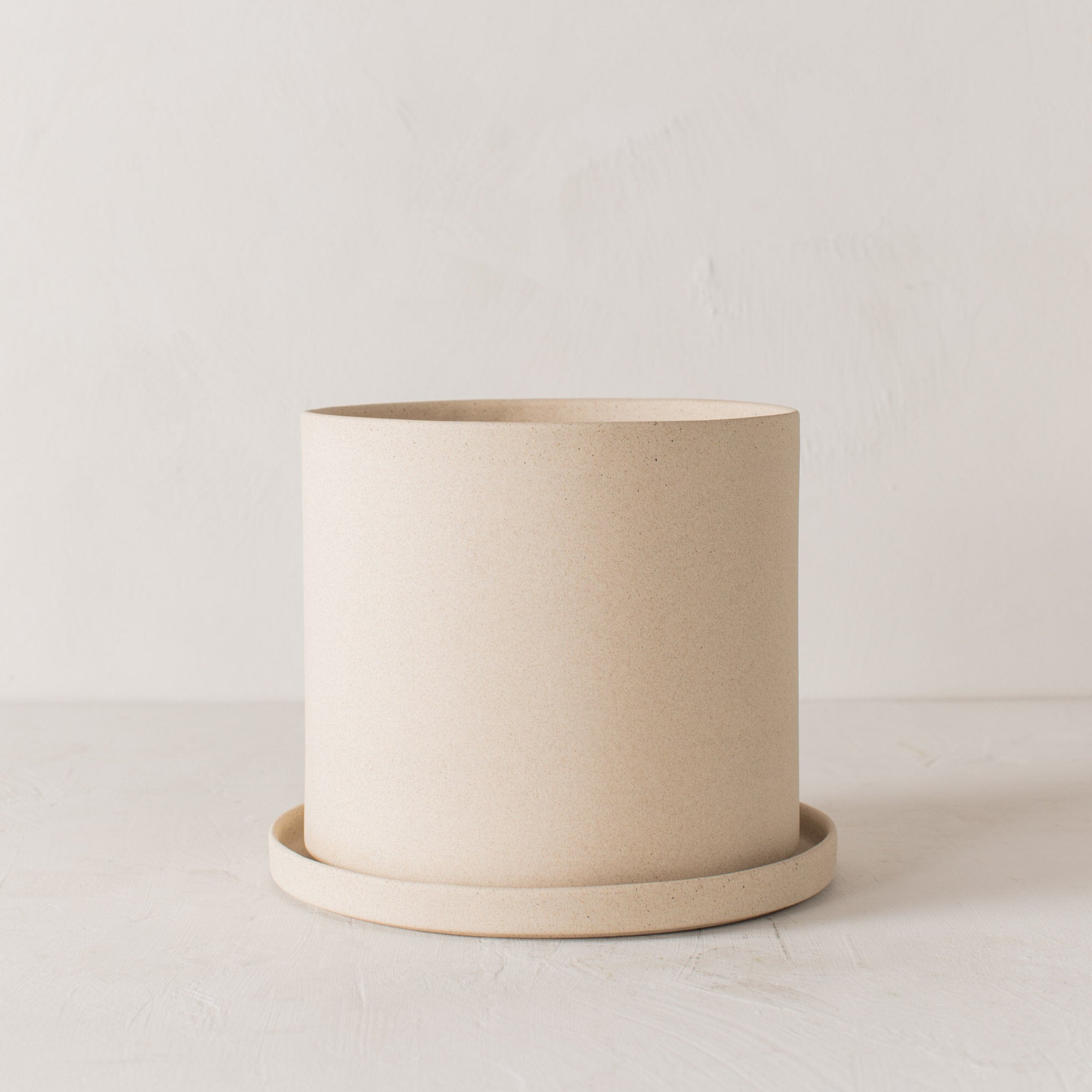 Stoneware 8 inch ceramic planter with bottom drainage dish. Staged on a white plaster textured tabletop against a plaster textured white wall. Designed by Convivial Production, sold by Shop Verdant Kansas City plant store.