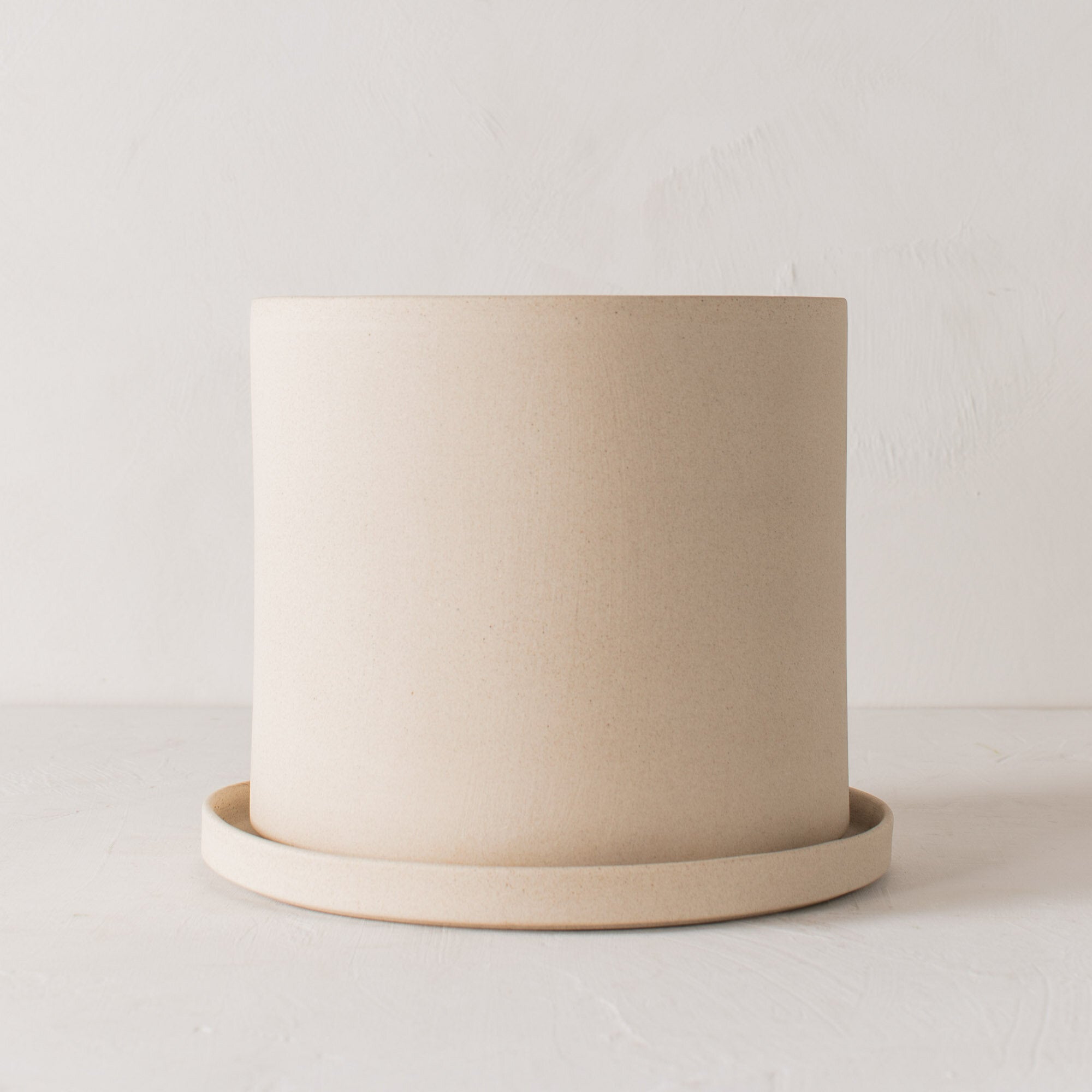 Stoneware 10 inch ceramic planter with bottom drainage dish. Staged on a white plaster textured tabletop against a plaster textured white wall. Designed and sold by Convivial Production, Kansas City Ceramics. 